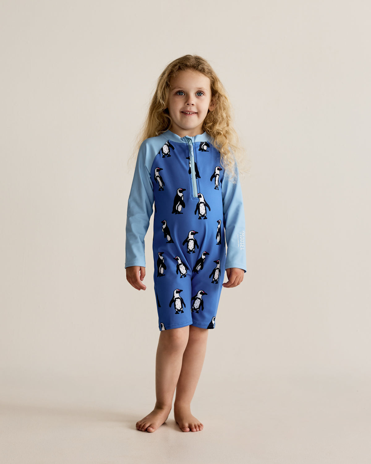 South African Boulders Beach Penguins water bird print on blue long-sleeve kids swimwear onesie, one-piece with UPF50+ sun protection and nylon fabric.