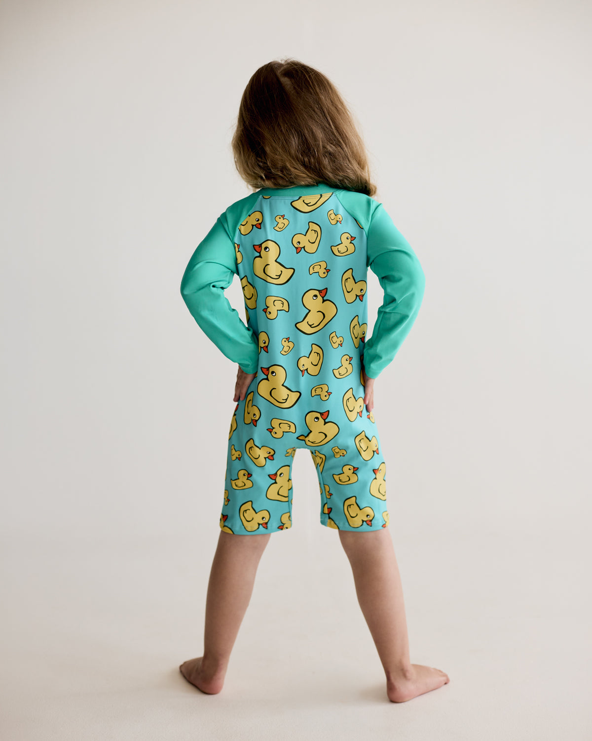 Yellow rubber ducks print on teal blue green long-sleeve kids swimwear onesie, one-piece with UPF50+ sun protection and nylon fabric.