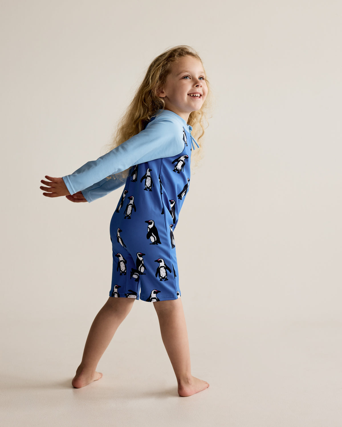 South African Boulders Beach Penguins water bird print on blue long-sleeve kids swimwear onesie, one-piece with UPF50+ sun protection and nylon fabric.